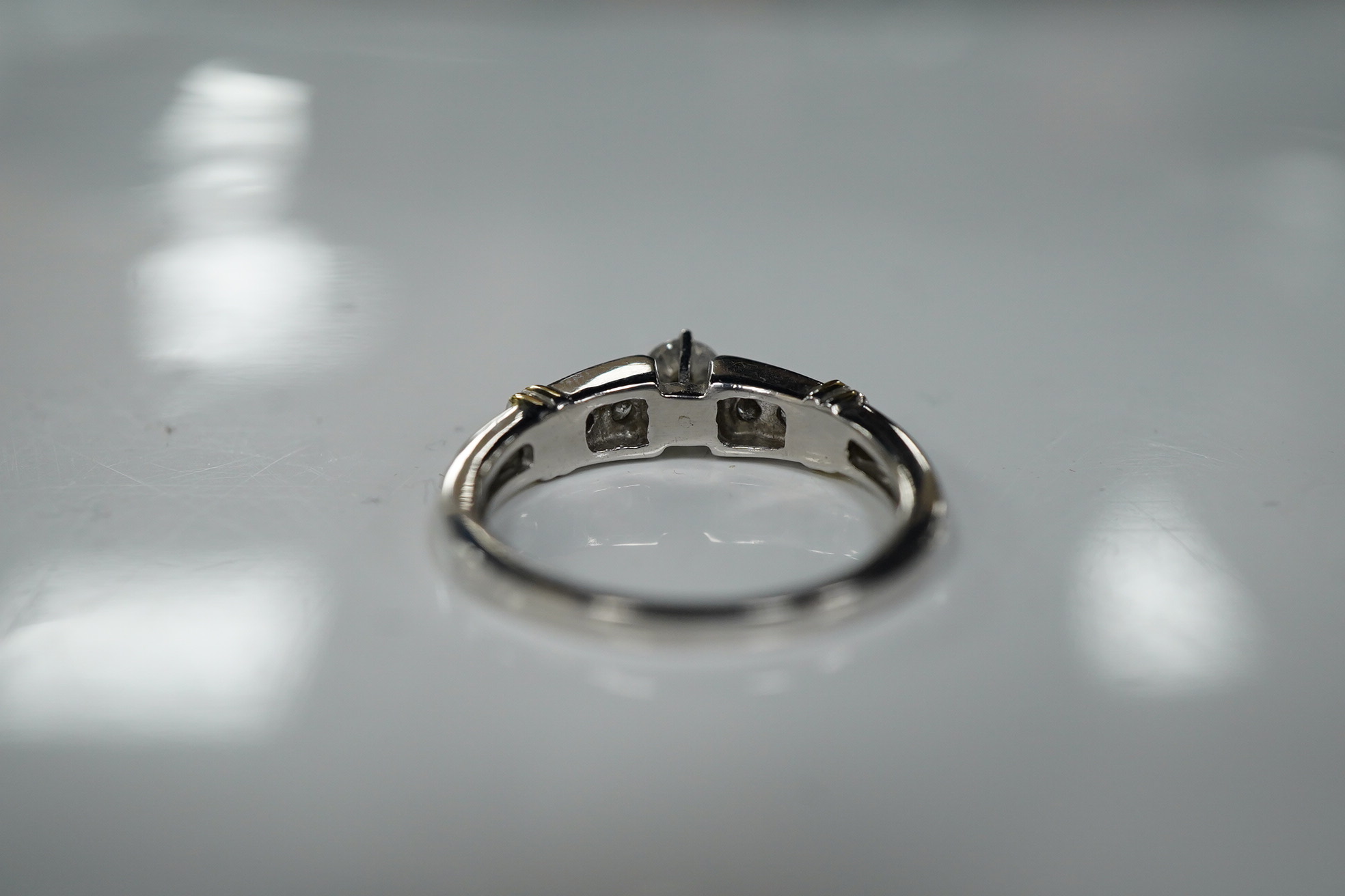 A diamond ring, claw-set with a brilliant-cut diamond weighing approximately 0.30 carats, to shoulders channel-set with smaller brilliant-cut diamonds, mounted in white gold, size R, stamped 14K, gross weight approximate